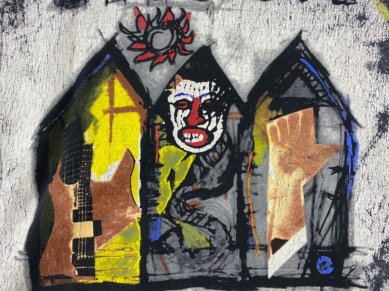 Puede incluir: Una camiseta negra y blanca con un dise&ntilde;o gr&aacute;fico abstracto de colores. El dise&ntilde;o presenta una cara con la nariz y la boca rojas, una guitarra y una mano que se levanta. El dise&ntilde;o est&aacute; rodeado de un fondo negro y blanco.