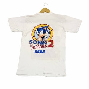 May include: White t-shirt with a blue Sonic the Hedgehog 2 Sega logo on the back. The logo features Sonic in a yellow circle with stars.