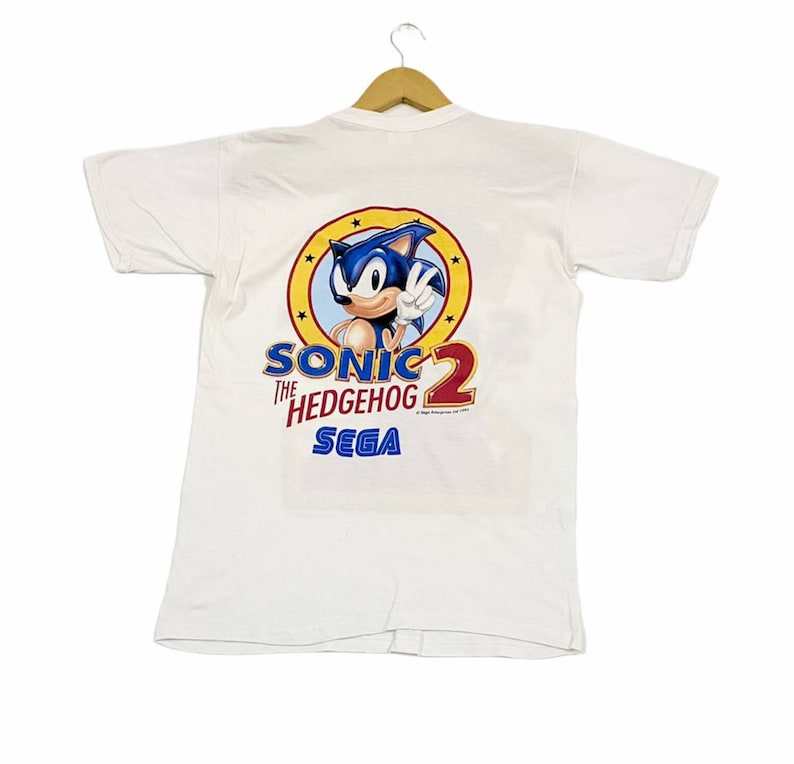 May include: White t-shirt with a blue Sonic the Hedgehog 2 Sega logo on the back. The logo features Sonic in a yellow circle with stars.