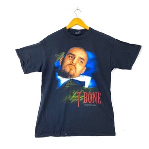 Puede incluir: Camiseta negra con un estampado gráfico de la cara de un hombre y el texto "T-Bone" en rojo.