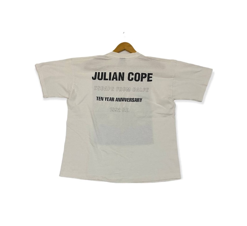 Pu&ograve; includere: Maglietta bianca con testo nero che recita "JULIAN COPE ESCAPE FROM BALFE TEN YEAR ANNIVERSARY 1992 CE."