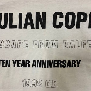 Pu&ograve; includere: Maglietta bianca con testo nero che recita "JULIAN COPE ESCAPE FROM BALFE TEN YEAR ANNIVERSARY 1992 C.E."