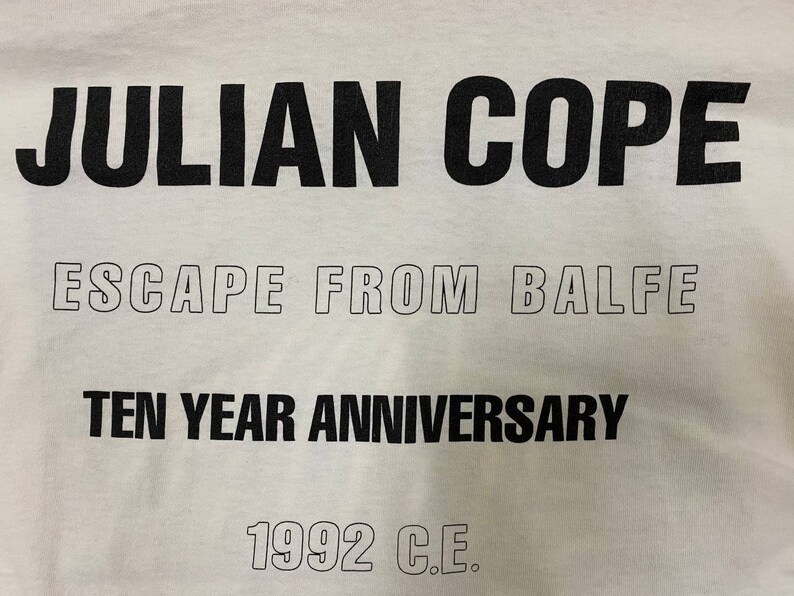 Pu&ograve; includere: Maglietta bianca con testo nero che recita "JULIAN COPE ESCAPE FROM BALFE TEN YEAR ANNIVERSARY 1992 C.E."