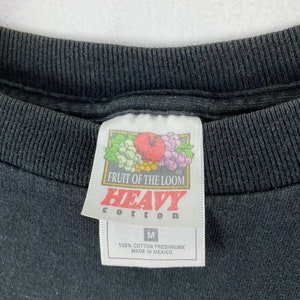 Może przedstawiać: Czarna metka koszulki Fruit of the Loom z białym tekstem, kt&oacute;ry brzmi "Heavy Cotton" i "100% Cotton Preshrunk Made in Mexico".