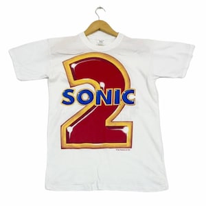 May include: White t-shirt with a large red and yellow graphic of the number "2" with the word "SONIC" in blue letters.