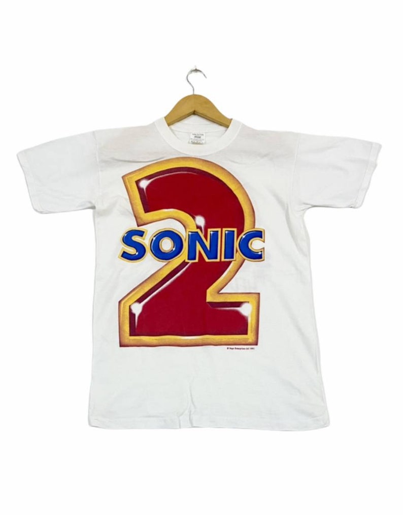 May include: White t-shirt with a large red and yellow graphic of the number "2" with the word "SONIC" in blue letters.