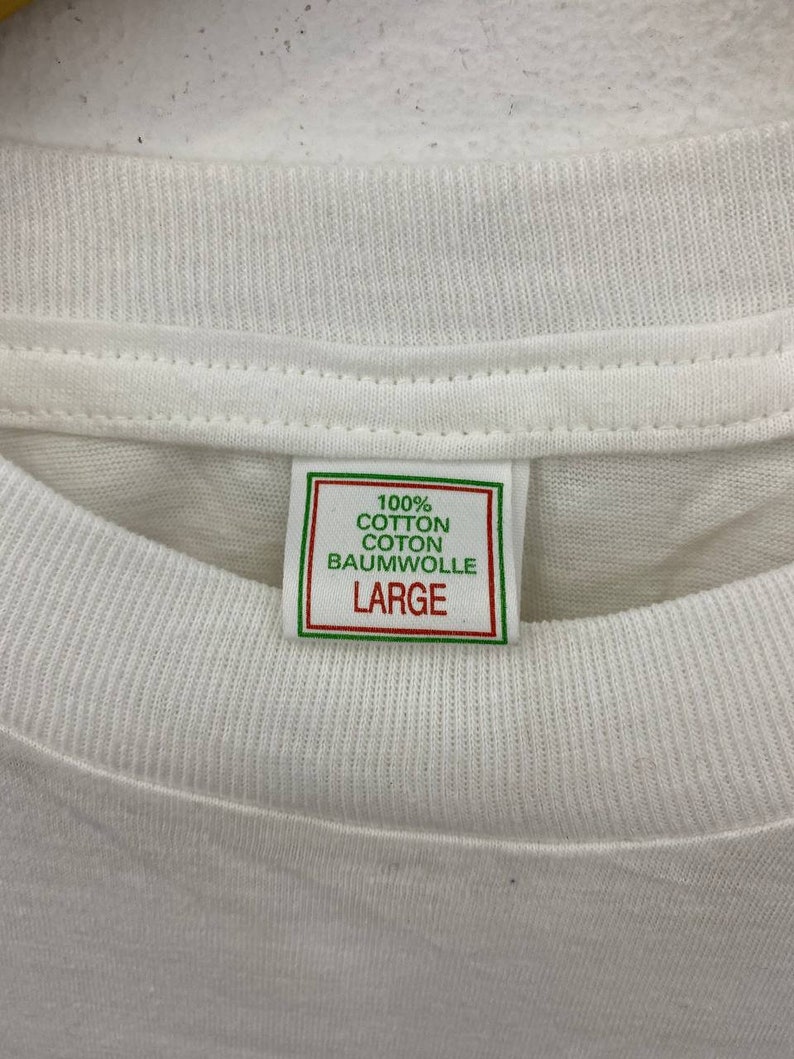 May include: White t-shirt with a green and white tag that reads "100% Cotton Coton Baumwolle Large"