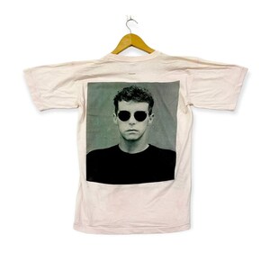 Puede incluir: Una camiseta rosa con una imagen en blanco y negro de un hombre con gafas de sol. El hombre mira directamente a la c&aacute;mara.