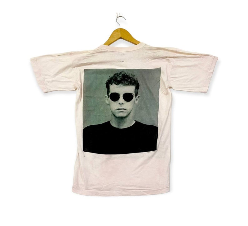 Puede incluir: Una camiseta rosa con una imagen en blanco y negro de un hombre con gafas de sol. El hombre mira directamente a la c&aacute;mara.