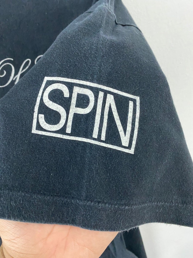 Puede incluir: Camiseta negra con texto blanco que dice "SPIN" en un cuadro.