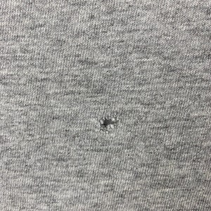 K&ouml;nnte beinhalten: Nahaufnahme eines grauen Stoffes mit einem kleinen Loch in der Mitte.