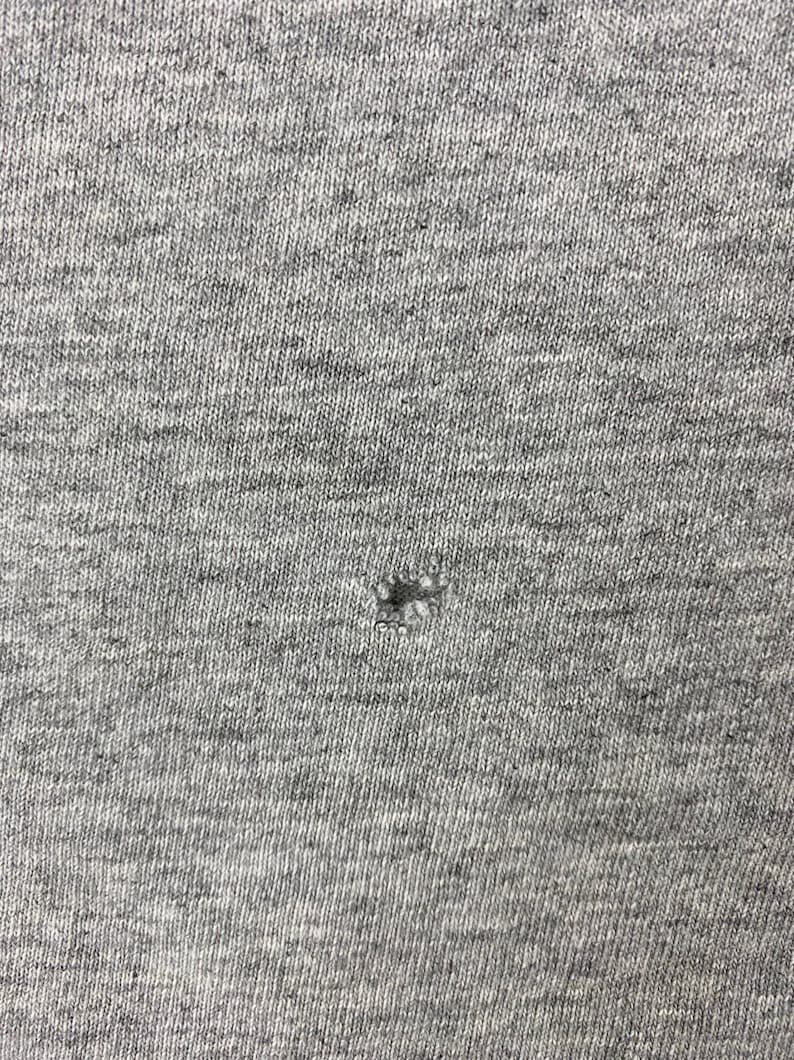 K&ouml;nnte beinhalten: Nahaufnahme eines grauen Stoffes mit einem kleinen Loch in der Mitte.