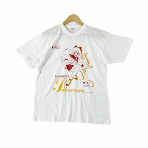 May include: White t-shirt with a red and white illustration of Sailor Venus from Sailor Moon. The text "Sailor Moon's Sailor Venus" is printed in yellow below the illustration.