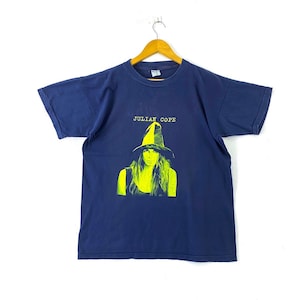 Può includere: Una maglietta blu navy con una grafica gialla di una donna che indossa un cappello. Il testo "JULIAN COPE" è stampato sopra la grafica.