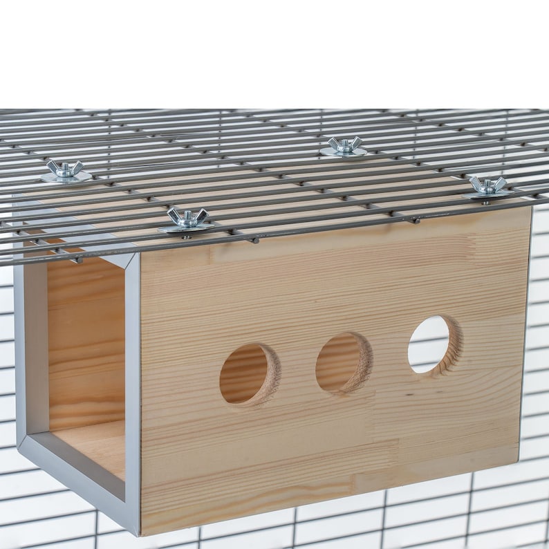 May include: A wooden hanging house for small pets, with three round openings and a light wood finish. The house is attached to a wire cage with metal nuts and bolts.