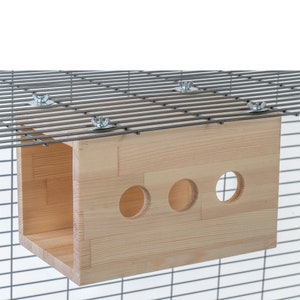 May include: A wooden hanging cage accessory for small pets, featuring three circular openings. The accessory is attached to a wire cage with metal nuts and bolts.