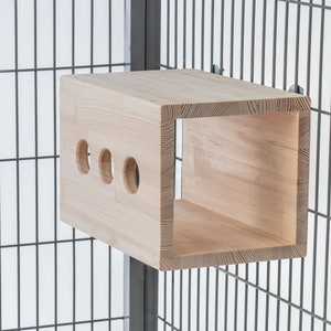 May include: A wooden cage accessory with a rectangular opening and three round holes. The accessory is made of light wood and is attached to a metal cage.
