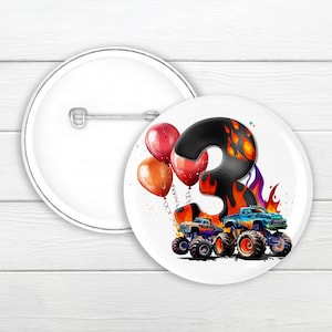 May include: A white button featuring a black and orange monster truck with flames and a number 3. Red and orange balloons are in the background.