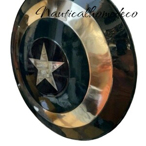 May include: A round, metal Captain America shield with a red, white, and blue design. The shield is painted black with a silver star in the centre.