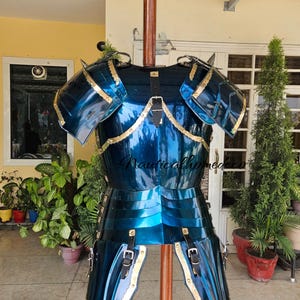 Op de afbeelding: Een blauw en gouden middeleeuws harnas met een decoratief ontwerp. Het harnas is gemaakt van metaal en heeft een glanzende afwerking. Het wordt getoond op een houten standaard.