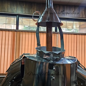 May include: A silver metal suit of armor with a conical helmet and a wooden pole. The helmet has a strap and a ring on the top. The suit of armor has a decorative design and is made of metal plates. The text "Nauticalhomedeco" is visible on the helmet and the suit of armor.