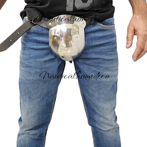 May include: A polished metal codpiece with a bear-like design, attached to a black leather belt. The item is worn over blue jeans. The text "Nauticalhomedeco" is visible on the image.