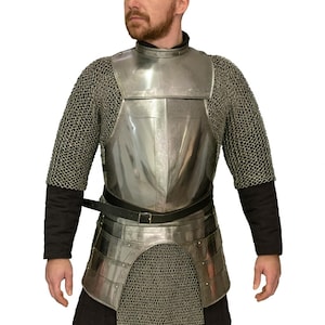 Könnte beinhalten: Eine mittelalterliche Rüstung mit einer polierten Brustplatte und Taillenpanzerung, Kettenärmeln und einem Kettenrock. Die Rüstung wird mit einem schwarzen Gürtel befestigt und über schwarzer Kleidung getragen.
