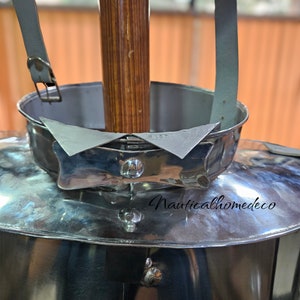 May include: Close-up of a silver helmet with a leather strap and a wooden pole. The helmet has a decorative band with a pointed design. The text "Nauticalhomedeco" is visible on the helmet.