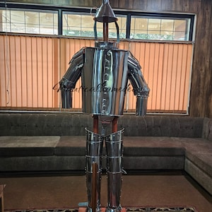 May include: A silver metal suit of armor with a helmet shaped like a funnel. The armor is standing on a wooden base with an axe next to it.