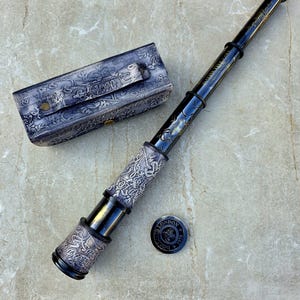 May include: A black and silver antique telescope with a matching leather case. The telescope has decorative engravings and the text "London 1920". A small, round emblem with the text "London" is also present.