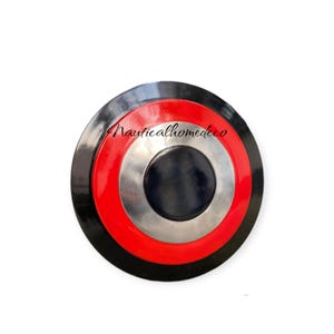 K&ouml;nnte beinhalten: Ein runder, schwarzer Metallschild mit einem konzentrischen Kreisdesign in Rot, Wei&szlig; und Schwarz. Der Schild hat eine silberne Mitte.