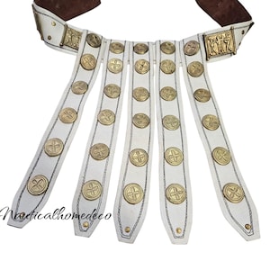 May include: White leather belt with a gold metal buckle and five straps with gold metal round accents. The buckle has a design of three figures.
