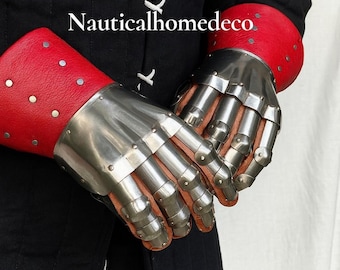 May include: A pair of medieval gauntlets with articulated metal plates and red leather cuffs. The gauntlets are designed to protect the hands and wrists. The text "Nauticalhomedeco" is visible in the image.