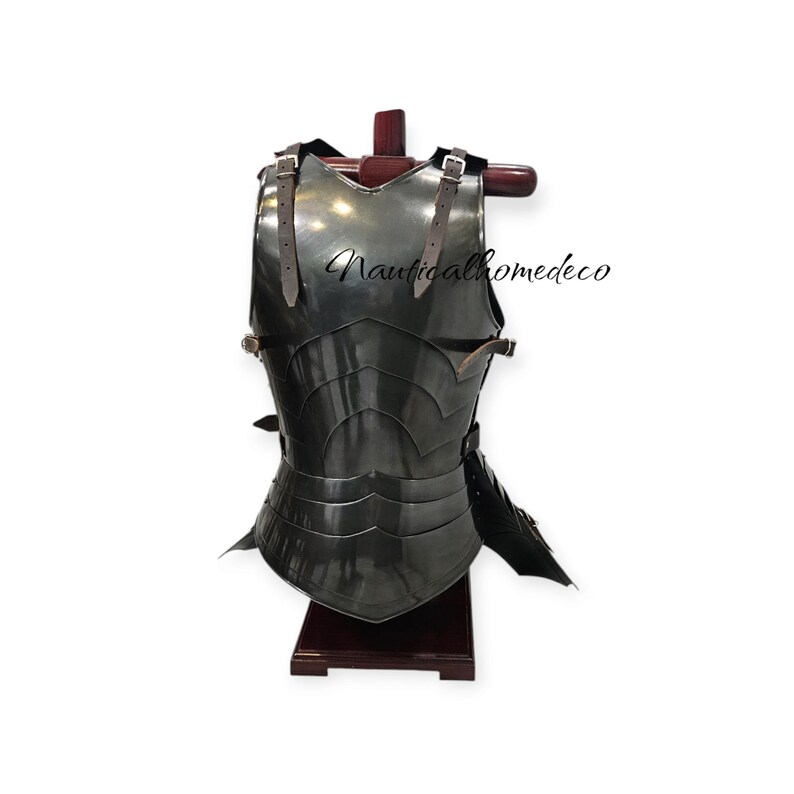 May include: A dark, metallic chest armor with layered plates and leather straps. The armor is displayed on a wooden stand. The text "Nauticalhomedeco" is visible on the armor.
