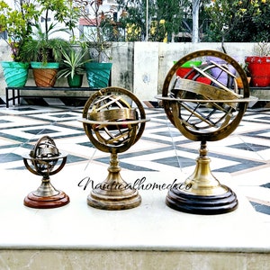 Puede incluir: Tres globos celestes de latón antiguo de diferentes tamaños sobre una superficie de mármol blanco. Los globos están detallados con líneas y marcas, y el globo más grande tiene una base de madera.