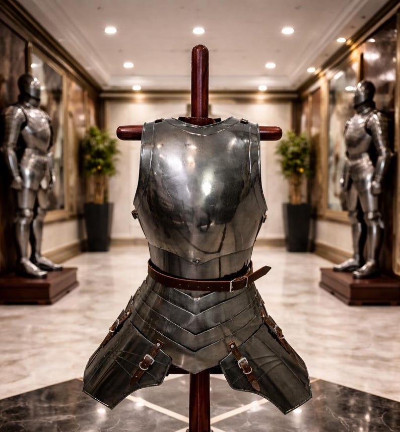 May include: A polished steel breastplate and faulds armor set displayed on a wooden stand. The armor features a brown leather belt and straps with buckles. Two full suits of armor stand in the background.