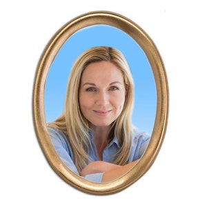 May include: A woman with blonde hair is smiling at the camera. She is wearing a light blue shirt and is sitting with her arms crossed. The photo is framed in a gold oval frame.