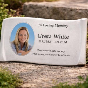 Puede incluir: Una lápida blanca con bordes redondeados, con un retrato de una mujer y la inscripción "In Loving Memory Greta White 9.9.1953 - 6.9.2024." También se incluye el texto "Your love will light my way, your memory will forever be with me."