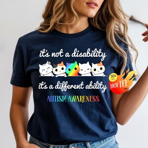 May include: Navy blue t-shirt with the text "it's not a disability, it's a different ability" and "AUTISM AWARENESS". The shirt features a row of cartoon cats in various colors. A sticker on the right says "20% off HOT TEE".
