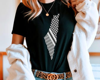 May include: A black short-sleeved t-shirt featuring a white graphic print of a map outline filled with a traditional keffiyeh pattern. The shirt is paired with light blue denim jeans, a leopard print belt with a gold double-ring buckle, and a white corduroy jacket.