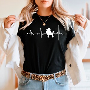 May include: A black t-shirt with a white silhouette of a poodle and a heartbeat graphic. The text "My Poodle My Heartbeat" is printed on the shirt.