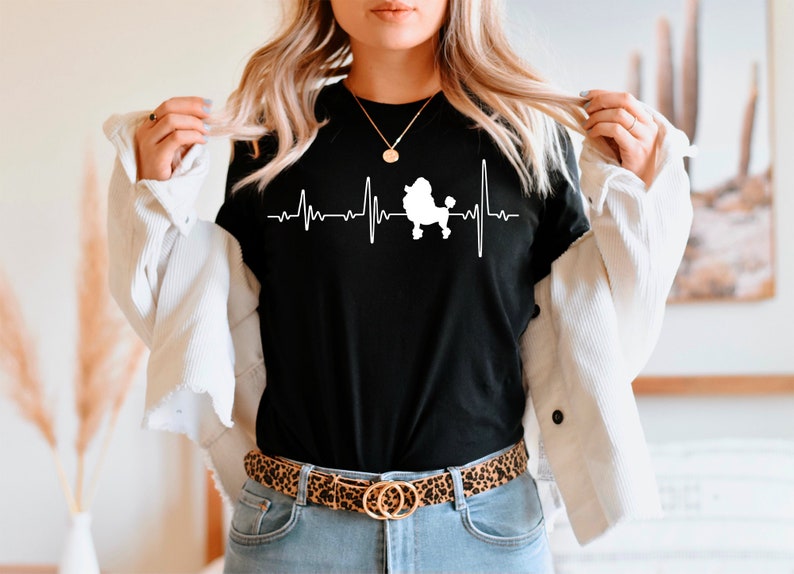 May include: A black t-shirt with a white silhouette of a poodle and a heartbeat graphic. The text "My Poodle My Heartbeat" is printed on the shirt.