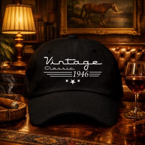 May include: Black baseball cap with the words "Vintage Classic 1946" in white script. The cap has a curved brim and a classic six-panel design. The background includes a lit lamp, a glass of red wine, and a cigar.