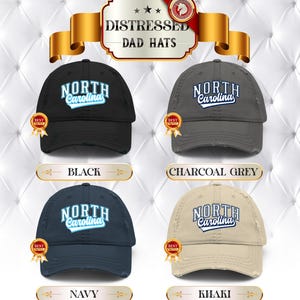 May include: Four distressed dad hats in black, charcoal grey, navy, and khaki. Each hat features the text "NORTH Carolina" in a stylized font. The hats have a worn, vintage look, with a "BEST" ribbon.