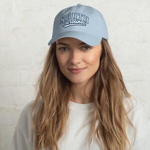 May include: Pale blue baseball cap featuring the text "NORTH Carolina" in white and navy blue. The cap has a curved peak and a classic six-panel design. The hat is made of a soft, durable fabric.