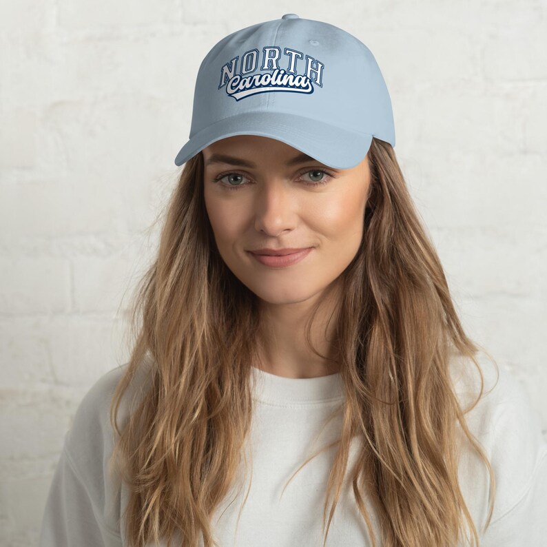 May include: Pale blue baseball cap featuring the text "NORTH Carolina" in white and navy blue. The cap has a curved peak and a classic six-panel design. The hat is made of a soft, durable fabric.