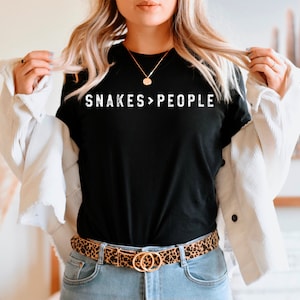 May include: A black t-shirt with the text "SNAKES>PEOPLE" in white lettering. The person is wearing a white jacket and a leopard print belt.