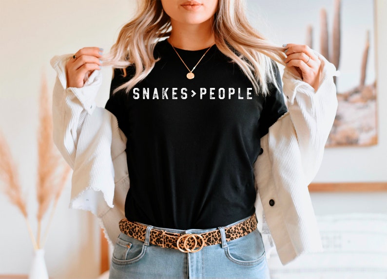 May include: A black t-shirt with the text "SNAKES>PEOPLE" in white lettering. The person is wearing a white jacket and a leopard print belt.