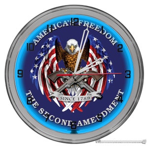 May include: A blue and silver wall clock with a neon blue ring around the edge. The clock face features an American bald eagle with crossed pistols, a banner that reads "Since 1789", and the text "America's Freedom The Second Amendment".