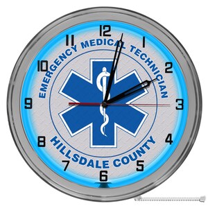 May include: A silver and blue neon clock with the words "Emergency Medical Technician Hillsdale County" and a blue star of life with a snake and staff symbol.